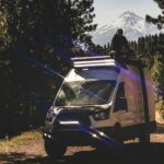 A man sitting on top of a van on a dirt road